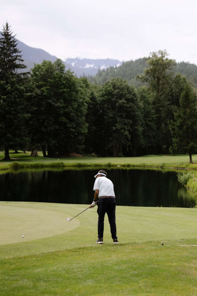 Golfer preparing to putt on scenic course with mountain views in background.